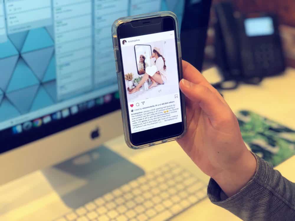 Person holding smartphone displaying Instagram post featuring influencer, with desktop computer in background, illustrating social media marketing strategies.